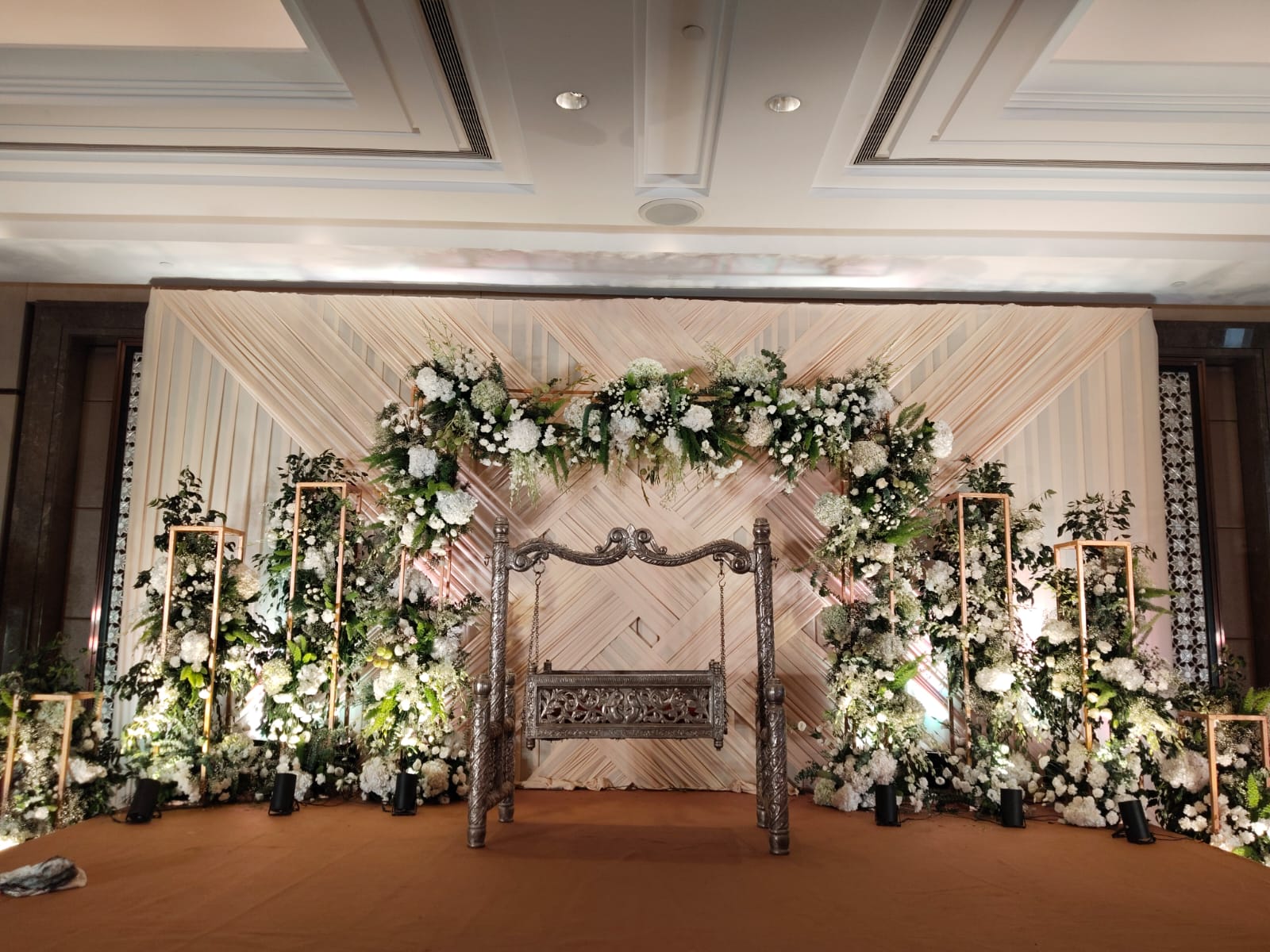 The Floral Swing Stage — A white floral arch framing a jhula stage, for a couple's reception.