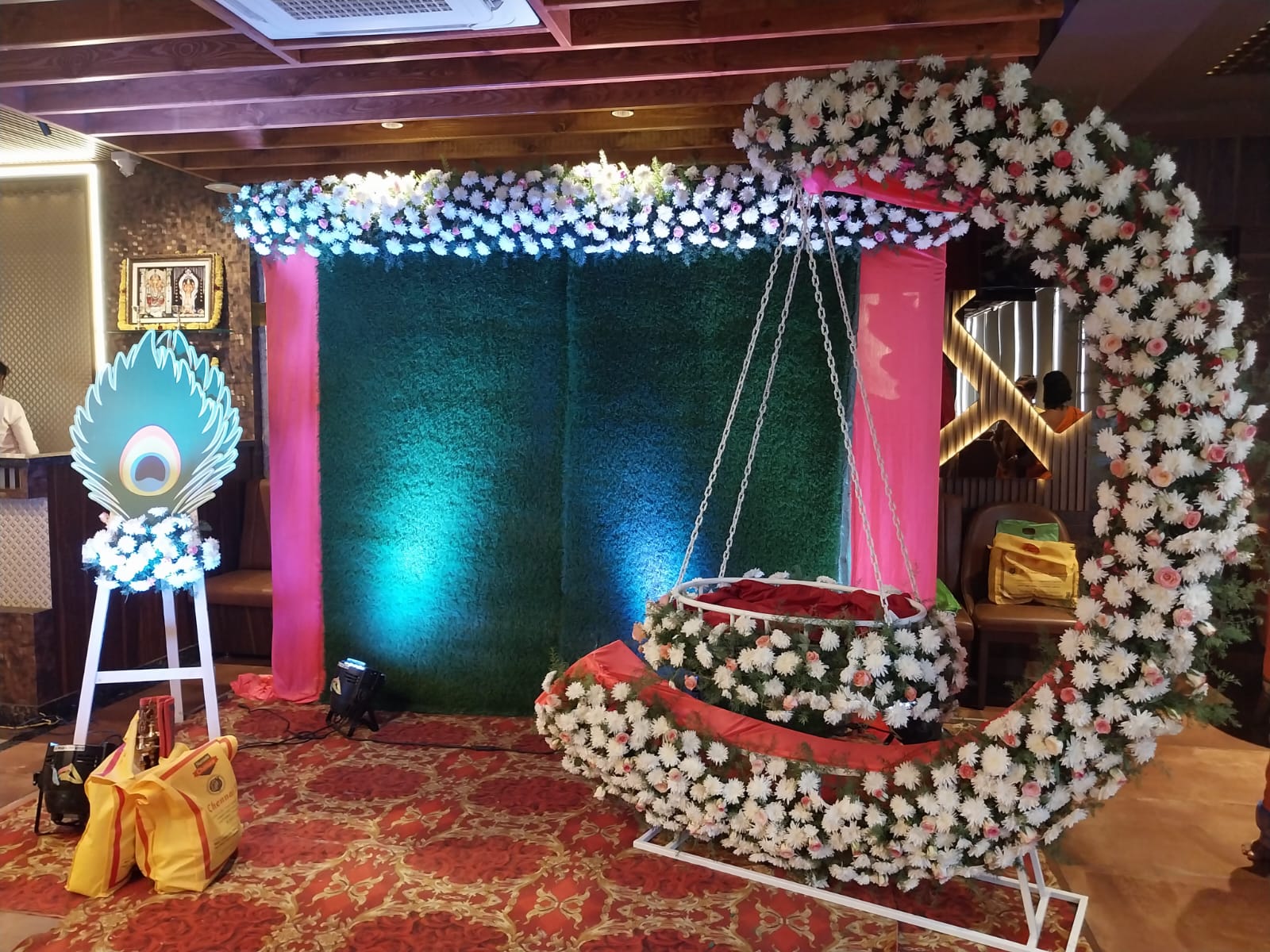 Pearl Jhula & Peacock — A pearl-white floral swing with a peacock accent, styled for a cradle ceremony.