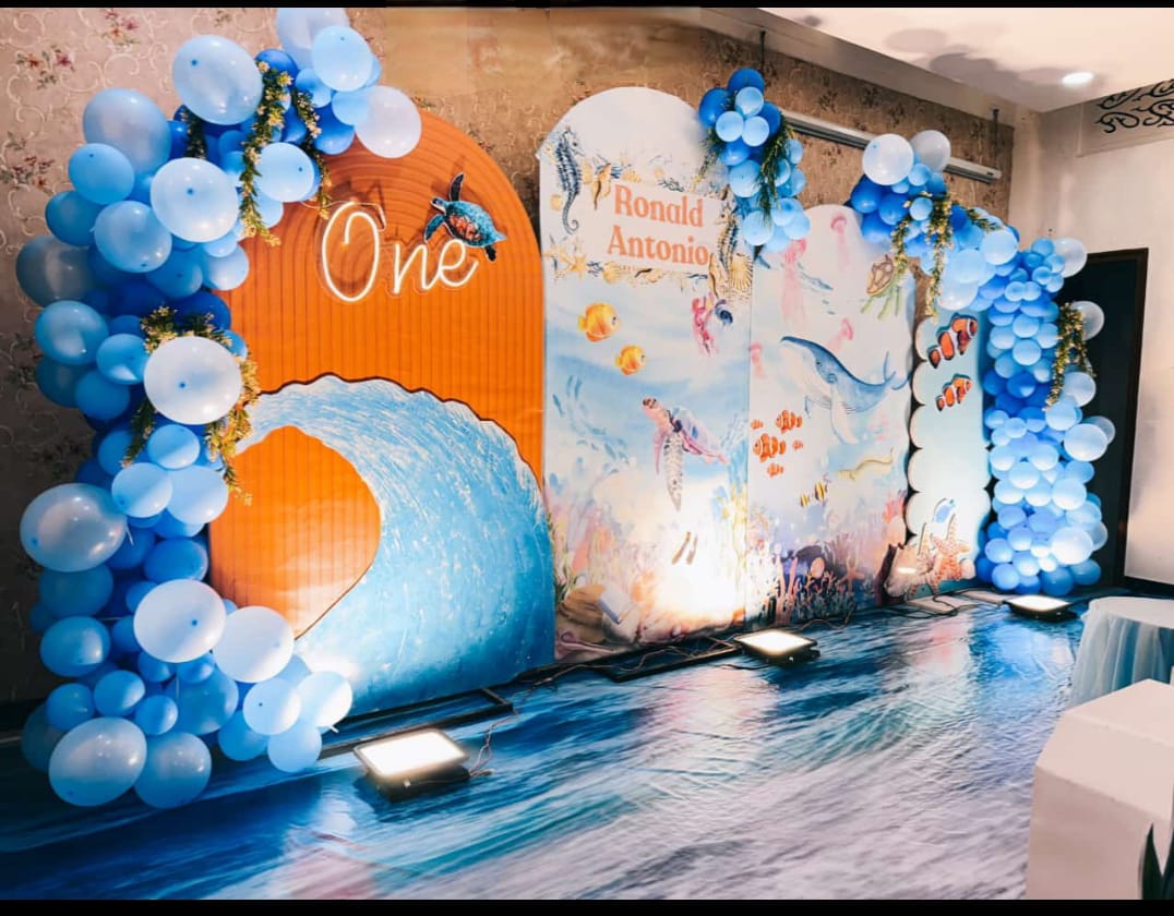 Under The Sea — An ocean-wave backdrop with blue balloon columns for a first birthday.